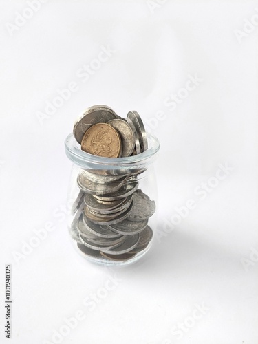 Bild auf Leinwand The photo shows a small glass container filled with coins, arranged in a haphaza