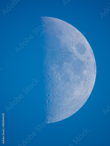 First-quarter moon is clearly visible against a bright blue daytime sky.