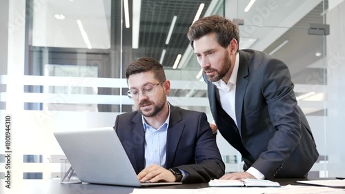 Boss advises subordinate worker. Businessman discussing with colleague at workplace using laptop computer in business office. Male manager consults, talking to employee. Executive explains work issue