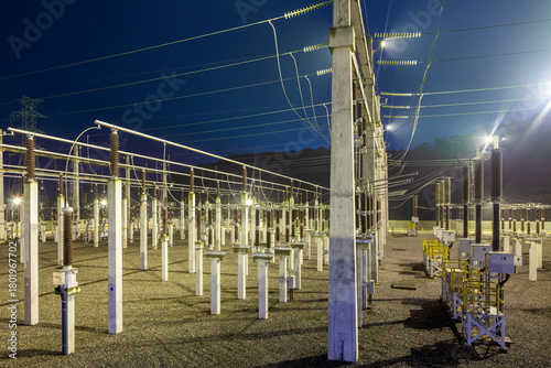 A nighttime view of a major electrical substation in Brazil, showcasing the complex network of high voltage insulators and wires.