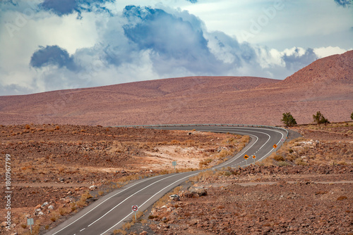 A paved highway winds through the desolate and rocky landscape of the Atacama Desert high plains near San Pedro de Atacama, Chile.