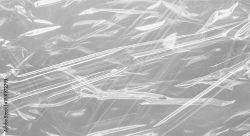 Transparent crinkled plastic film texture with light reflections and abstract lines over a smooth gray background