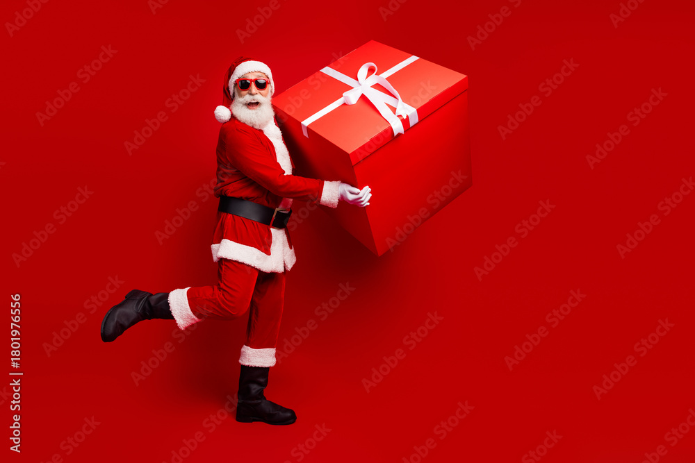 Naklejka premium Santa Claus joyfully holds a giant red gift box against a vibrant festive background, celebrating the essence of Christmas holiday cheer.