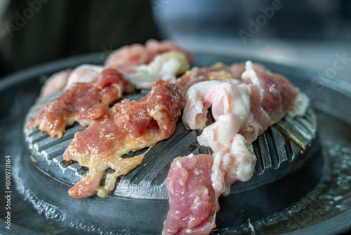 Close-up of Thai-style barbecue grill pan, known as Moo Kratha, with pork belly, shrimp, and vegetables cooking on a hot grill and soup. Popular Asian dining experience in Thailand.
