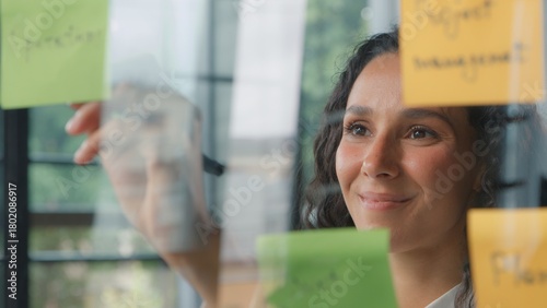 Hispanic woman office business worker write sticky notes writing stickers data information businesswoman female girl creating corporate project tasks working thinking about job plans on glass board