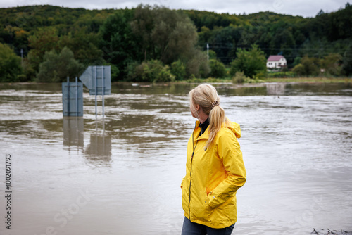 Flooded river. Worried woman looking at overflowing water during flood. Extreme weather and natural disaster