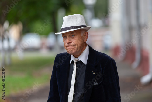 Stylish older man walks down the street wearing a hat and suit, capturing a moment of sophistication and reflection