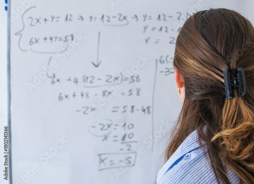 Teacher explaining complex algebraic equations on whiteboard during a math lesson, instructing students on solving problems and understanding mathematical concepts in education environment