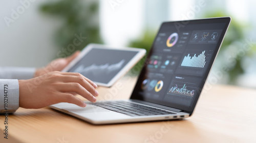 Focused business person analyzing financial data on laptop and tablet computer. screen shows chart, graph, and statistics for marketing and strategy planning in office
