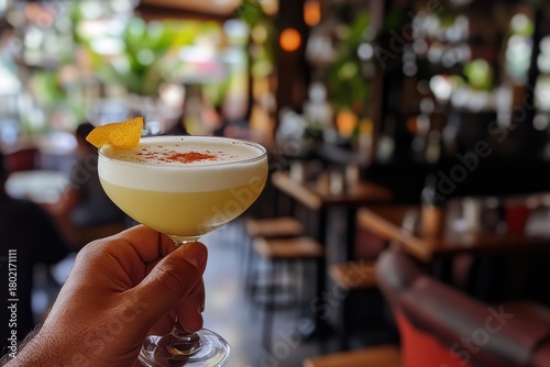A person is holding a glass of a yellow drink with a slice of orange in it