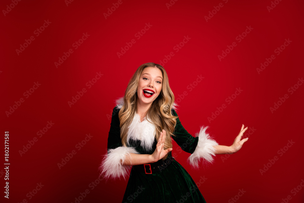 Naklejka premium Cheerful christmas fashion portrait of a smiling woman in a green fur trimmed dress against a bold red background conveying festive glamour