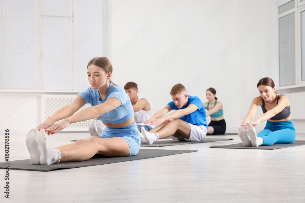 Naklejka premium Group of people doing stretching exercise on fitness mats in gym