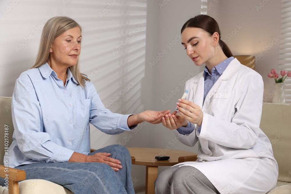 Fototapeta premium Diabetes. Doctor checking patient's blood sugar level with lancet pen on armchair indoors