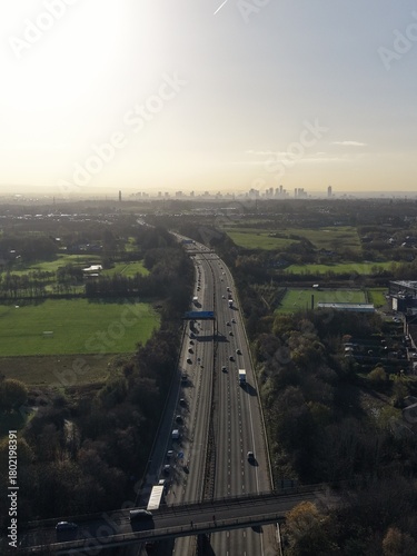 Aerial view of busy traffic on a motorway with view of Manchester skyline in the distance. Silhouette image with low sun. 