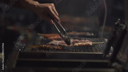 Slow motion showing a street food chef grilling skewers over hot charcoal at a yatai stall in Fukuoka, Japan, with glowing heat and smoke rising in the dark