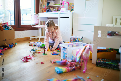 Little girl sitting on the floor in her bedroom and playing with toys