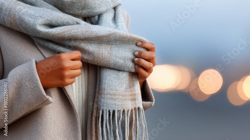 Person arranging light gray woven scarf while standing outdoors with copy space