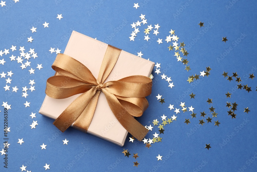 Obraz premium Decorated Christmas gift and confetti on blue background, top view