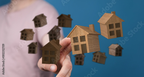 Fotografija A hand holding up wooden houses, symbolizing property investment, real estate market, homeownership, and housing