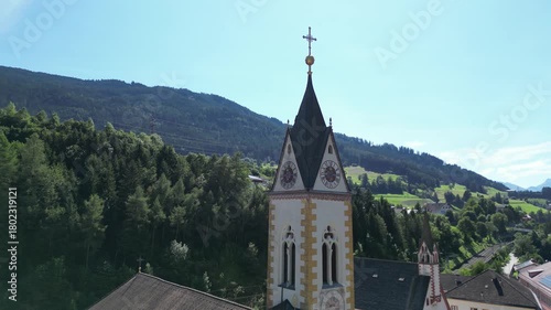 church steeple detail in austria near brenner pass scenic small town in the alps with mountain background river train tracks alpine village christian cross top colorful white drone footage scene 