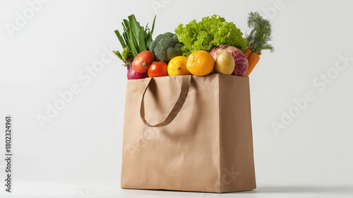 Fototapeta Naklejka Na Ścianę i Meble -  brown paper grocery bag is brimming with colorful fresh produce including greens, citrus fruits, and root vegetables against a clean white background