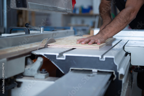 Ein Handwerker schneidet eine Holzplatte mit einer Kreissäge in einer Werkstatt. Fokus auf die Hand und das Holz, industrielle Umgebung, keine Gesichter sichtbar.