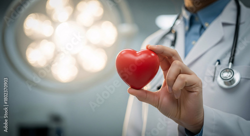 Doctor holding a red heart in his hand wearing a white coat and a stethoscope in a hospital room
