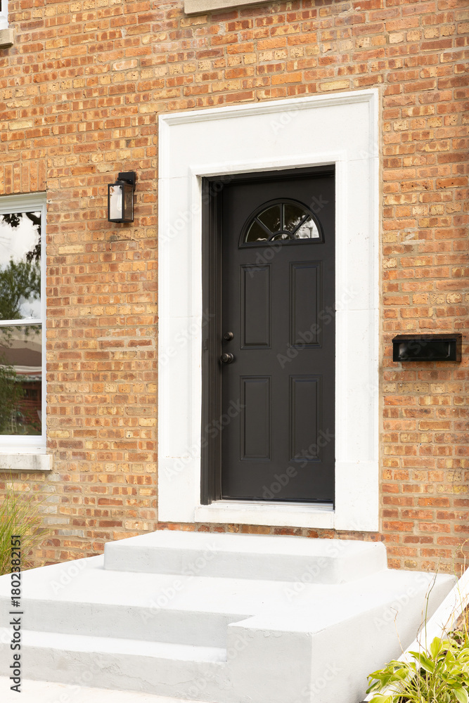 Fototapeta premium A front door detail on a brick home with concrete steps leading to a black door and white door frame.