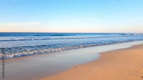Serene ocean waves gently lap against a warm sandy beach under a clear blue sky, creating a peaceful coastal landscape