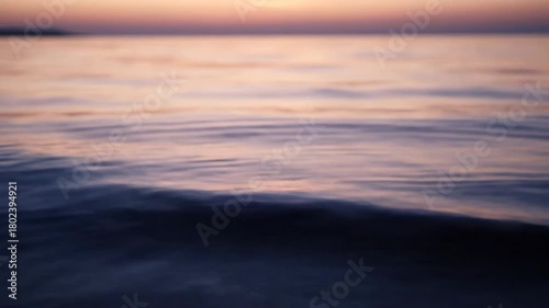 Tranquil ocean waves gently lap at a secluded shore during a soft, ethereal sunset, painting the sky in hues of lavender and gold