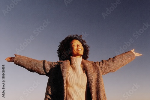 Joyful woman with open arms embraces freedom under vast sky at sunset