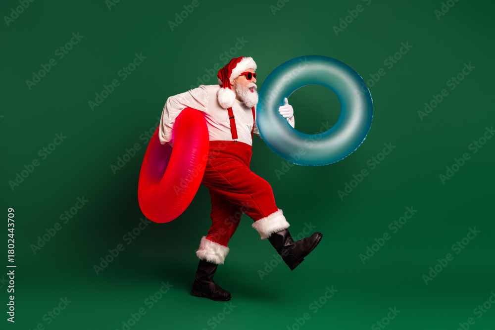 Obraz premium Santa in red costume with two inflatable rings strikes a playful pose against a green background perfect for christmas themed stock