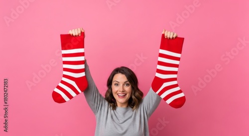 Woman holding up Christmas stockings with a joyful expression on pink background