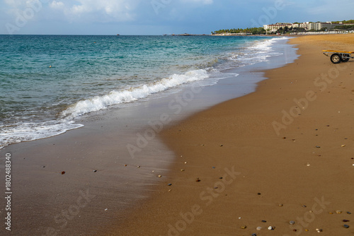 Fototapeta Naklejka Na Ścianę i Meble -  Calm turquoise sea with white surf line on yellow sandy beach under partly cloudy sky, showing distant resort umbrellas and palms during season's final warm days. Sorgun, Antalya, Turkey.


