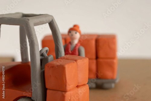 Miniature clay warehouse workers operating forklift with orange boxes in small warehouse scene