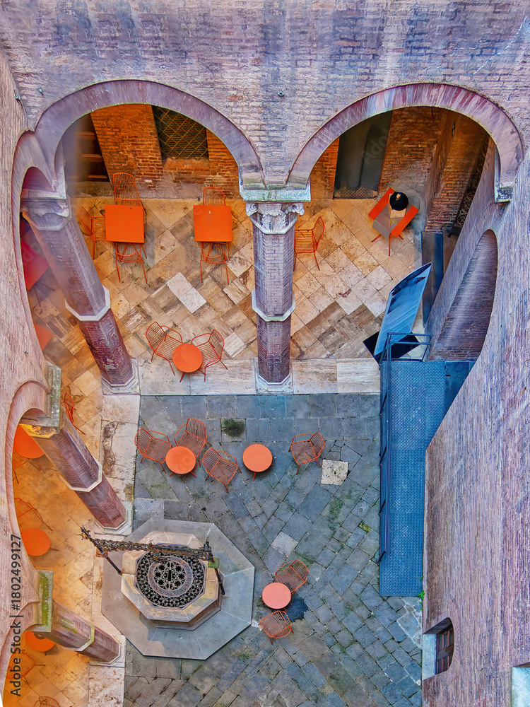 Fototapeta premium Aerial view of the Palazzo delle Papesse courtyard in Siena, Italy — warm terracotta arches and orange café tables create a striking harmony between Renaissance stone and modern design.