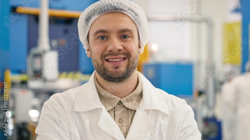 Close up portrait of Caucasian male worker in protective hairnet smiling and looking directly at camera. Standing in industrial factory environment. Modern manufacturing background indoors.
