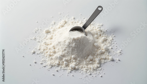 Heap of monohydrate creatine powder with a measuring scoop on a white surface
