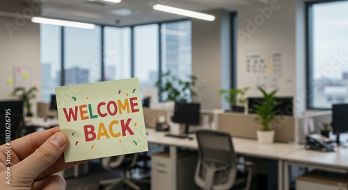 Office note with lettering WELCOME BACK, blurred office desks on background. Workspace with sign for collegues, greetings after sick leave or vacation. Selective focus