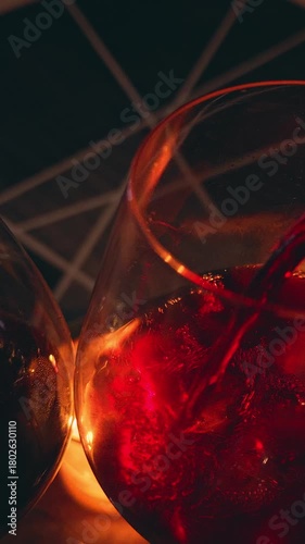 Vertical video. Bottle Pouring Red Wine into Glass Near Candlelight Creating Deep Red Glow and Warm Ambience, Romantic Celebration Concept
