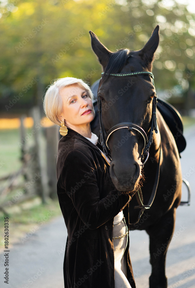 Obraz premium An adult rich woman standing in a park and holding a brown luxury horse