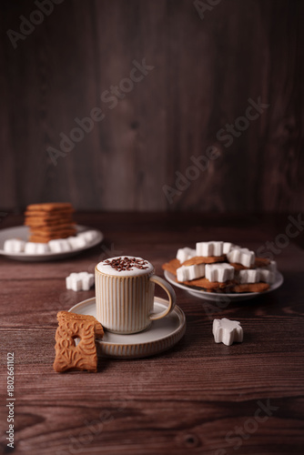 cozy coffee moment with a ceramic mug of frothy cappuccino, topped with chocolate shavings, paired with biscuits and sugar shapes on warm wooden table, stylized, elegant, simple, stack, marshmallow
