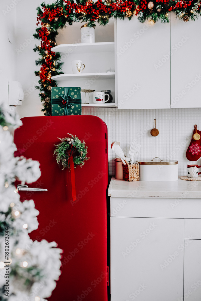 Fototapeta premium Festive kitchen featuring a red refrigerator, a pine cone wreath, red ornaments, creating a warm holiday atmosphere. Selective focus