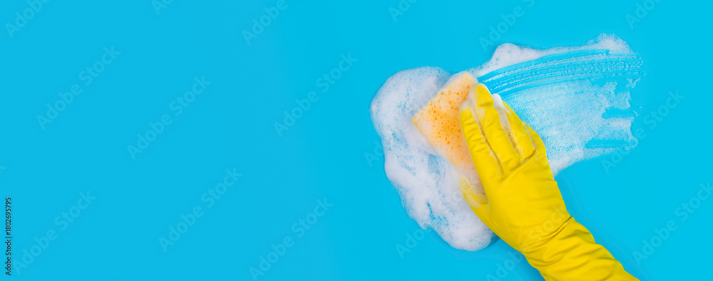 Obraz premium Hand in Yellow Glove Holds Sponge and Wipes Soapy Foam on Blue Background