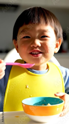 Young child eating meal with spoon and bowl indoors brightly lit with natural sunlight healthy eating