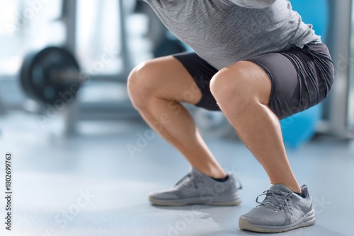 Faceless person performing controlled squat during knee recovery bright gym environment injury rehabilitation concept