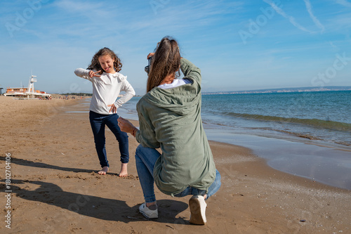 A girl is posing for a picture with her friend on the beach. The girl is wearing a white shirt and jeans