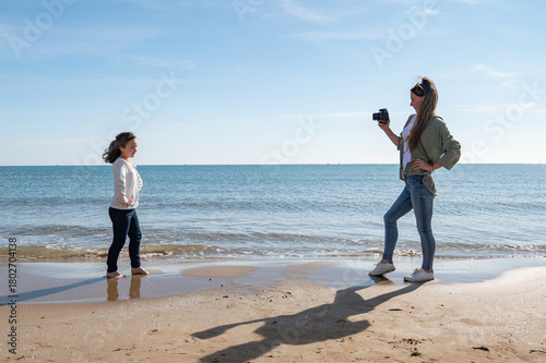 A girl is posing for a picture with her friend on the beach. The girl is wearing a white shirt and jeans