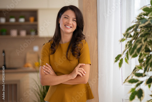 A smiling woman standing with folded arms at home.  
