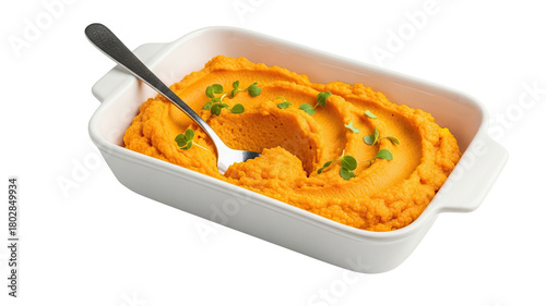 Creamy orange vegetable puree, possibly from carrots or sweet potatoes, served in a white ceramic baking dish with a spoon and garnished with fresh microgreens, isolated on black